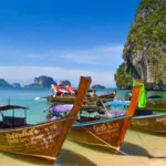 Longtail boats moored on a beach beneath a limestone cliff in Thailand